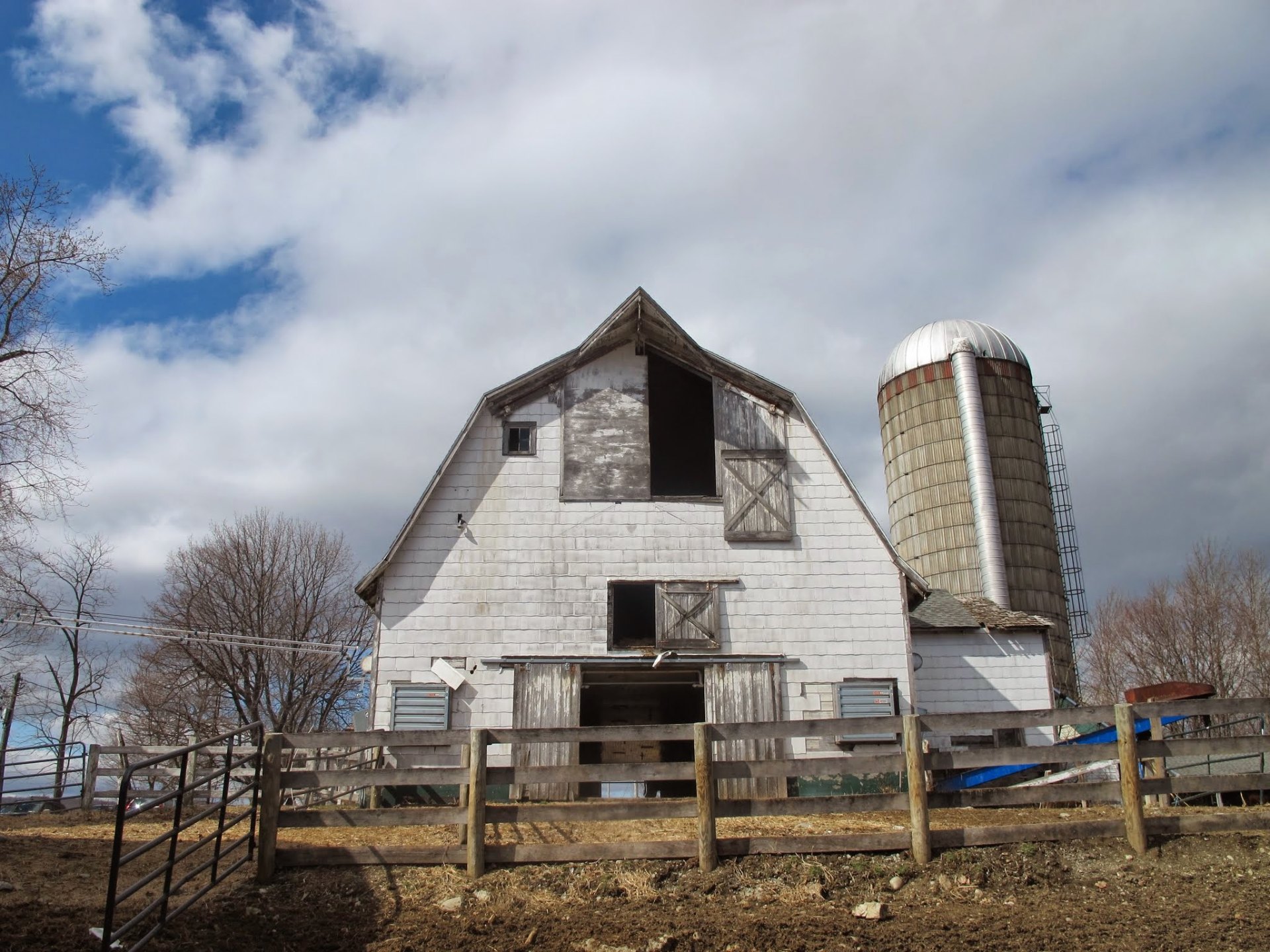 A weathered white barn with silo against a bright cloudy sky